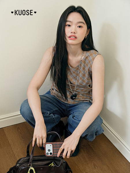 Model wearing a plaid sleeveless top and jeans with a handbag.