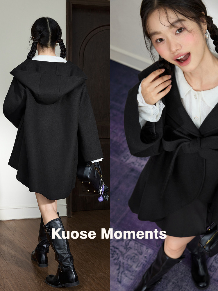 Model wearing a black hooded cape-style coat over a white blouse with black boots