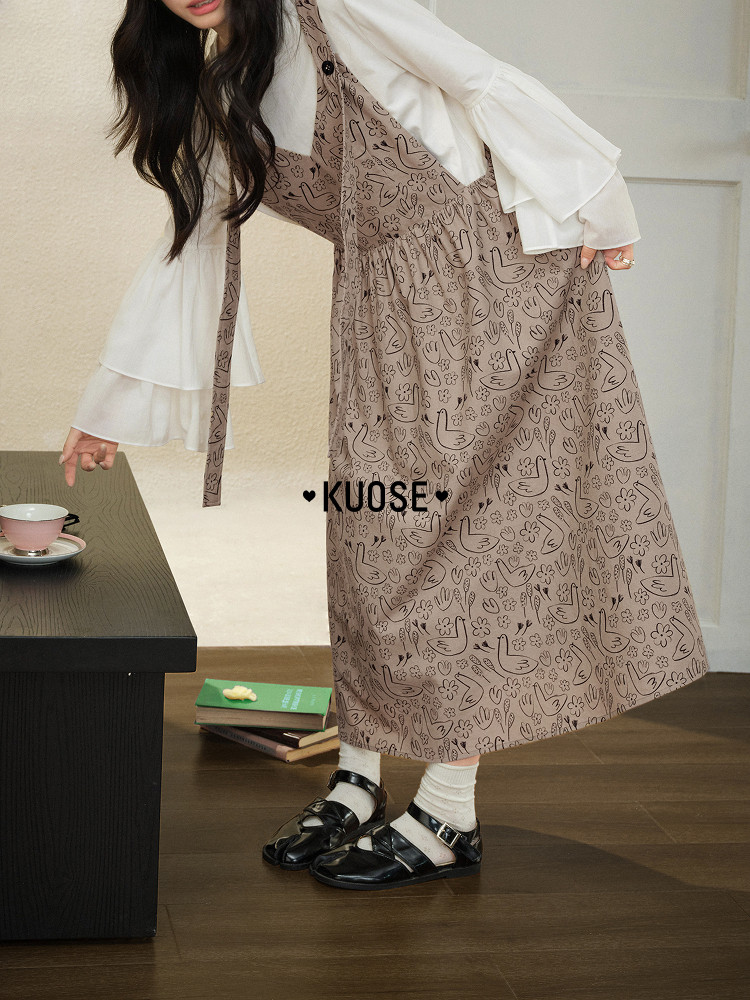 Model wearing a patterned brown pinafore dress over a white blouse