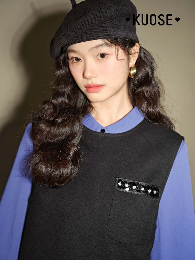Model wearing a black sleeveless vest over a blue shirt with a black beret