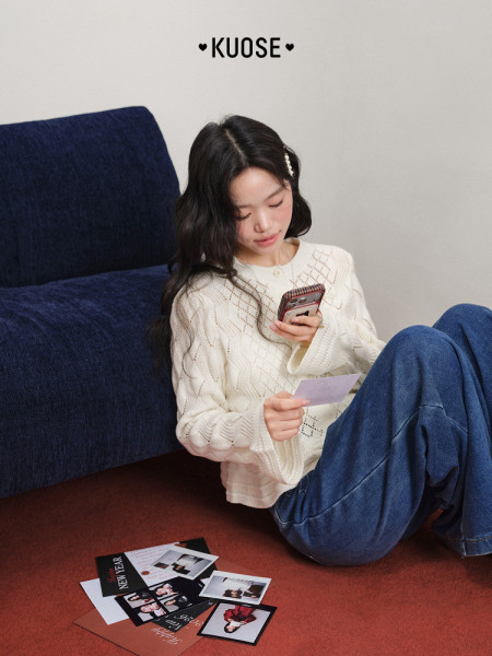 Woman wearing a white knit sweater and blue jeans while sitting indoors