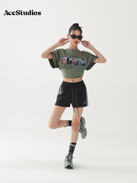 Model wearing an olive graphic crop tee with black athletic shorts and sneakers