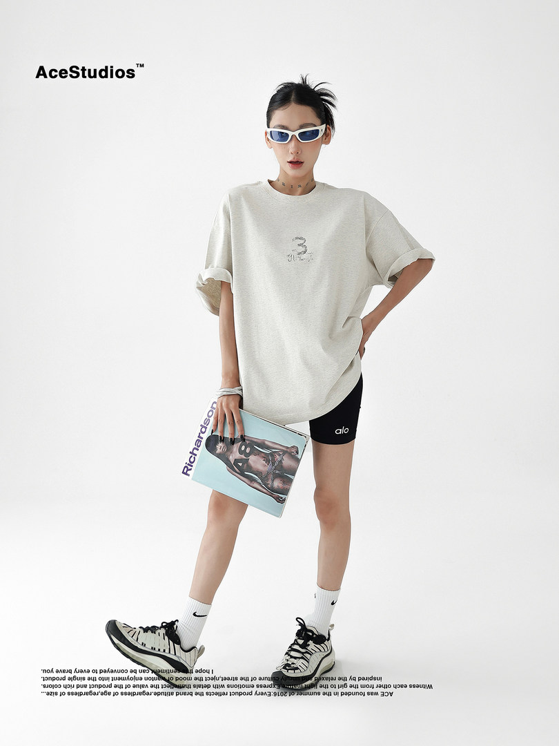 Model wearing an oversized light gray T-shirt with black shorts and sneakers