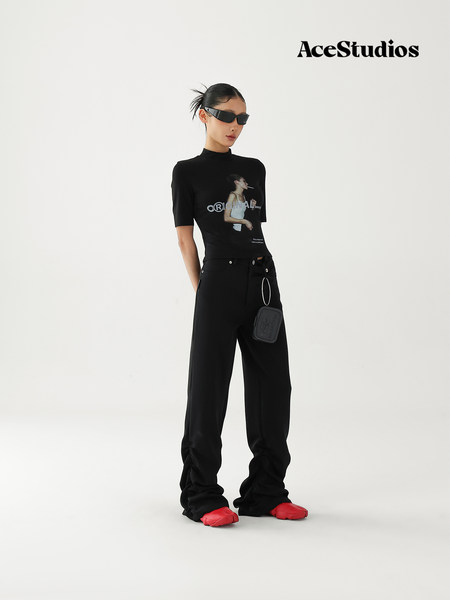 Model wearing a black graphic top with wide-leg black pants and red shoes