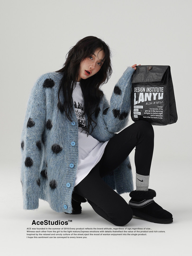 Model wearing a fuzzy blue polka dot cardigan with black leggings and a printed tote bag.