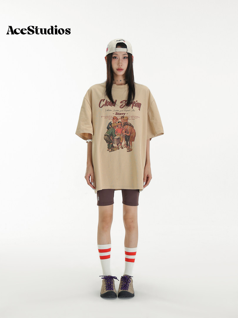 Model wearing an oversized beige graphic T-shirt with shorts, cap, and sneakers