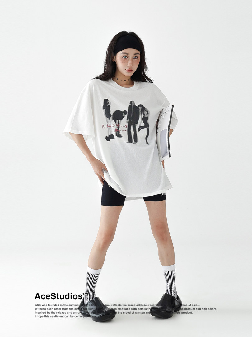 Model wearing an oversized white graphic T-shirt with black shorts and socks