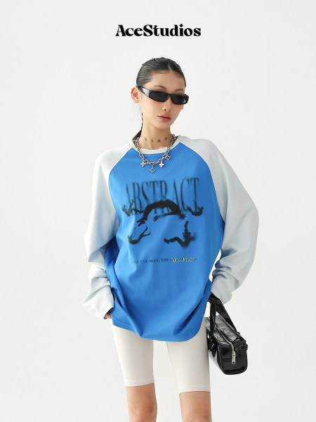Model wearing a blue and white graphic long-sleeve top with a black handbag