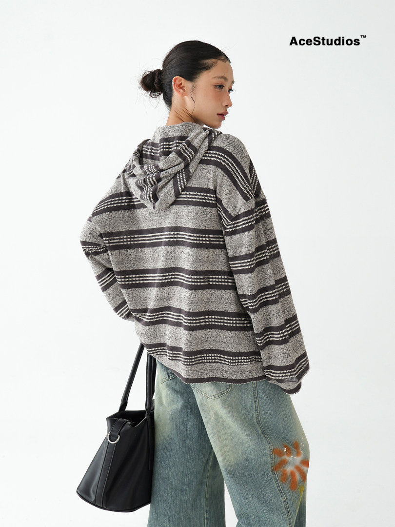 Model wearing a striped oversized hooded sweater with wide-leg jeans and a black tote bag.