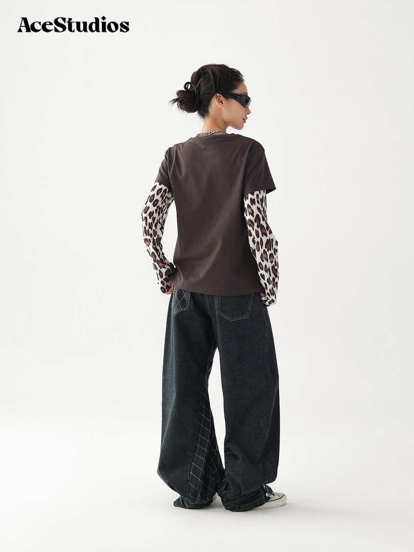 Model wearing a layered streetwear outfit with graphic long sleeves, dark tee, and baggy jeans