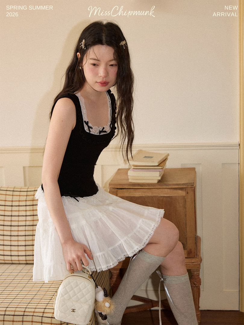Model wearing a black and white lace-trim dress with a small quilted handbag