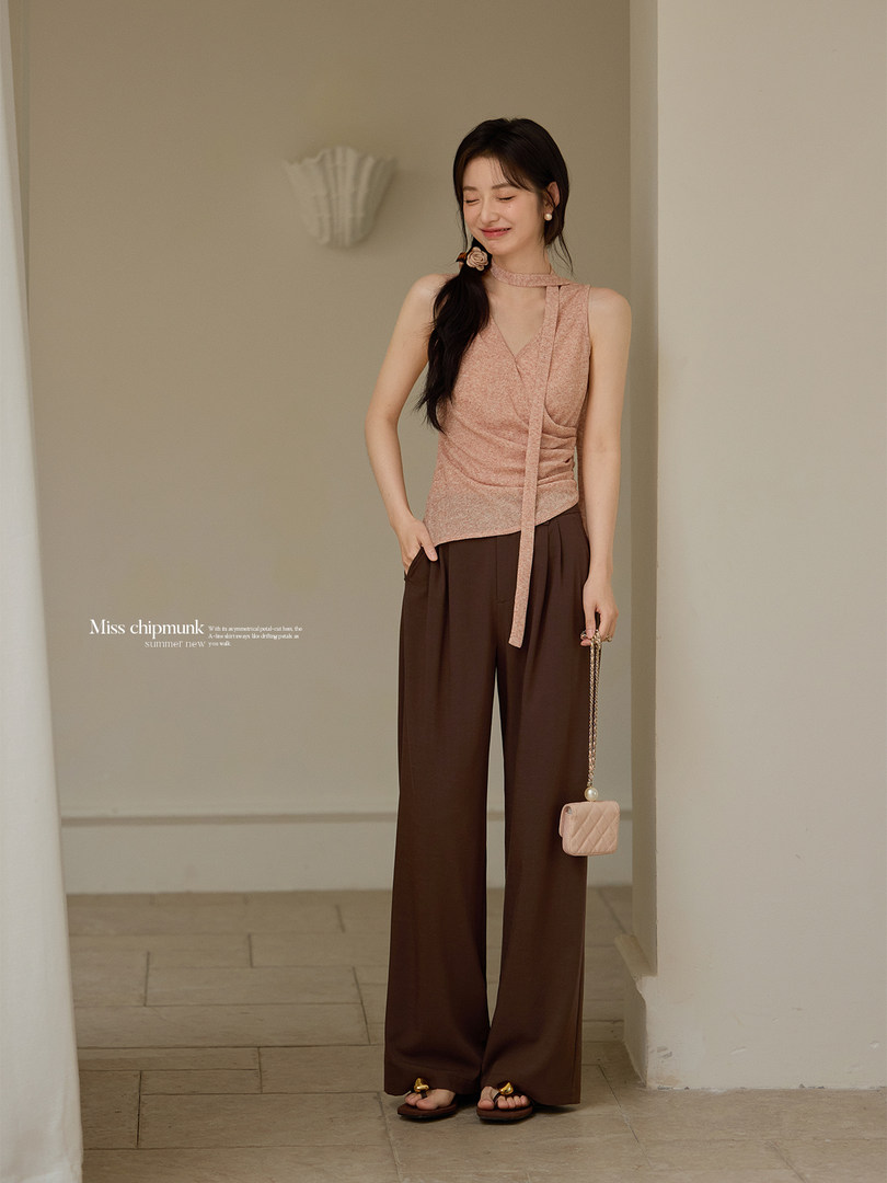 Woman modeling a sleeveless pink top with wide brown pants and a small quilted handbag