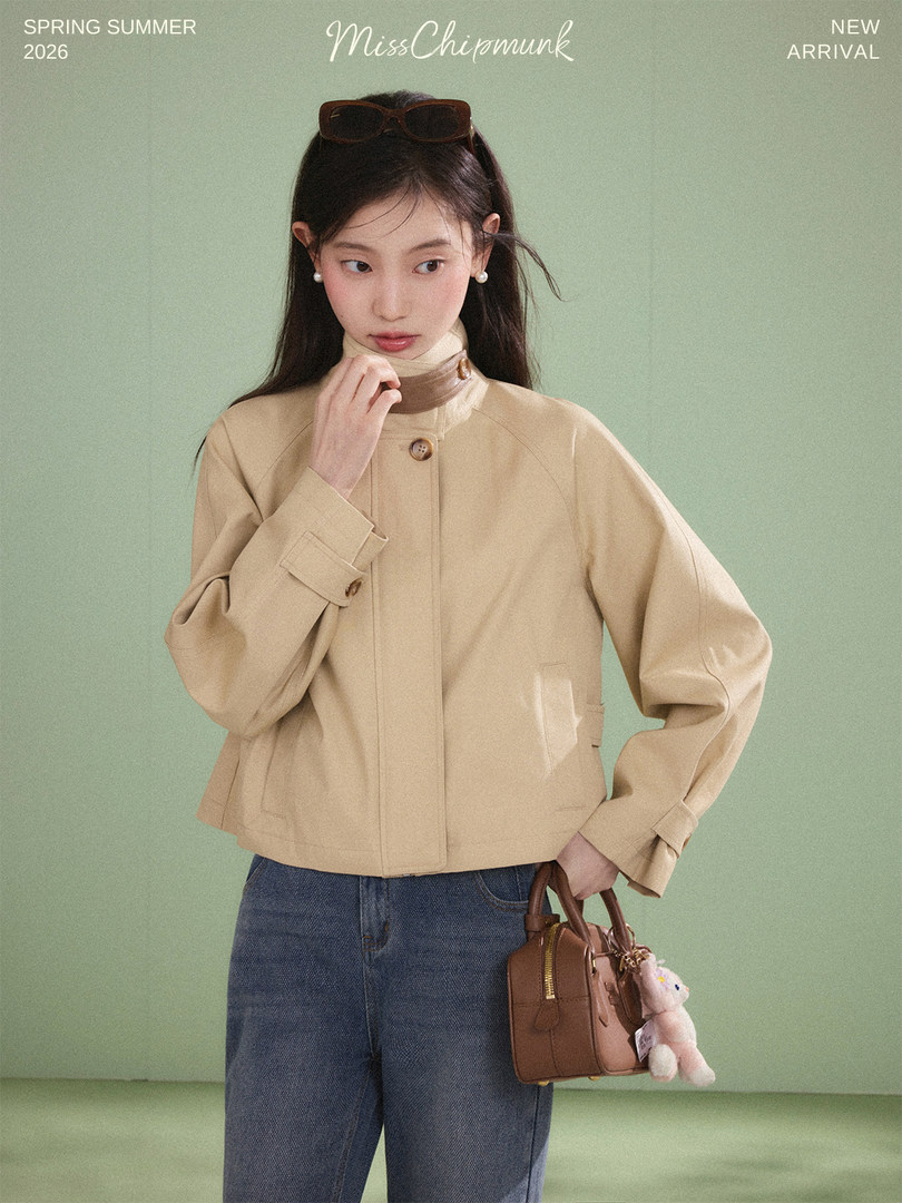 A model wearing a beige cropped jacket with blue jeans and holding a small brown handbag.