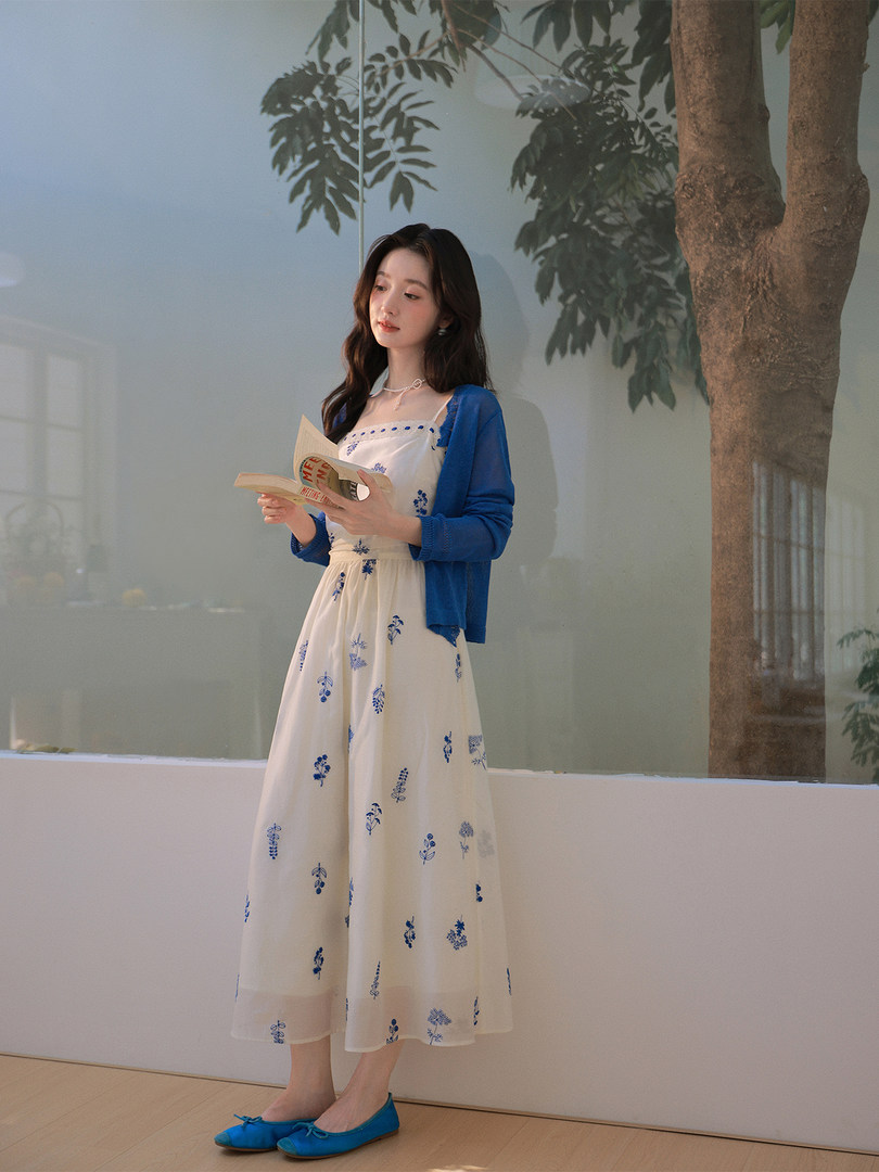 Woman wearing a white floral dress with a blue cardigan and blue flats