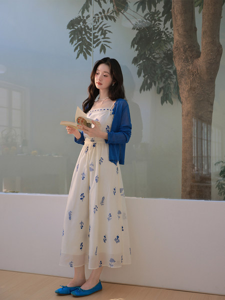 Woman wearing a white floral dress with a blue cardigan and blue flats