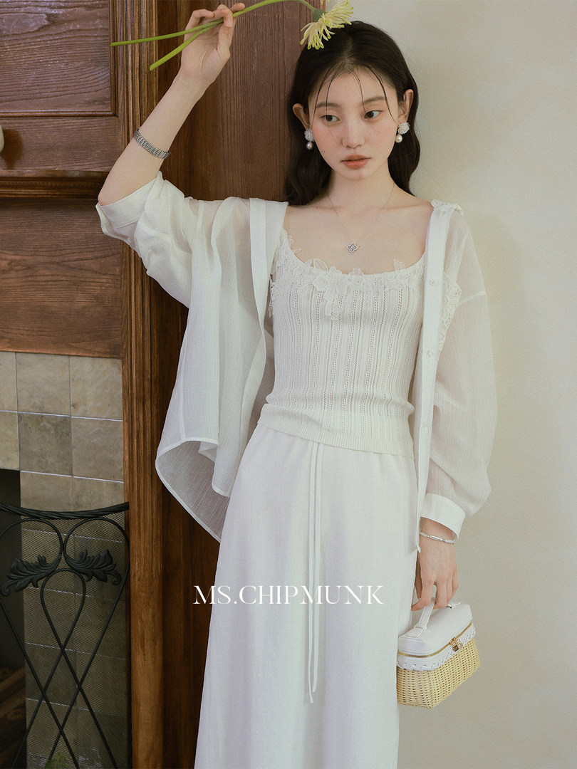 Model wearing a white sheer cardigan and lace-trim dress set with a small woven handbag