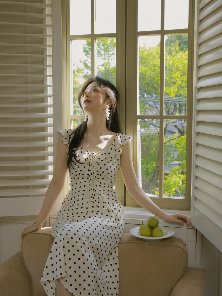 Woman wearing a white polka dot ruffled dress by a window