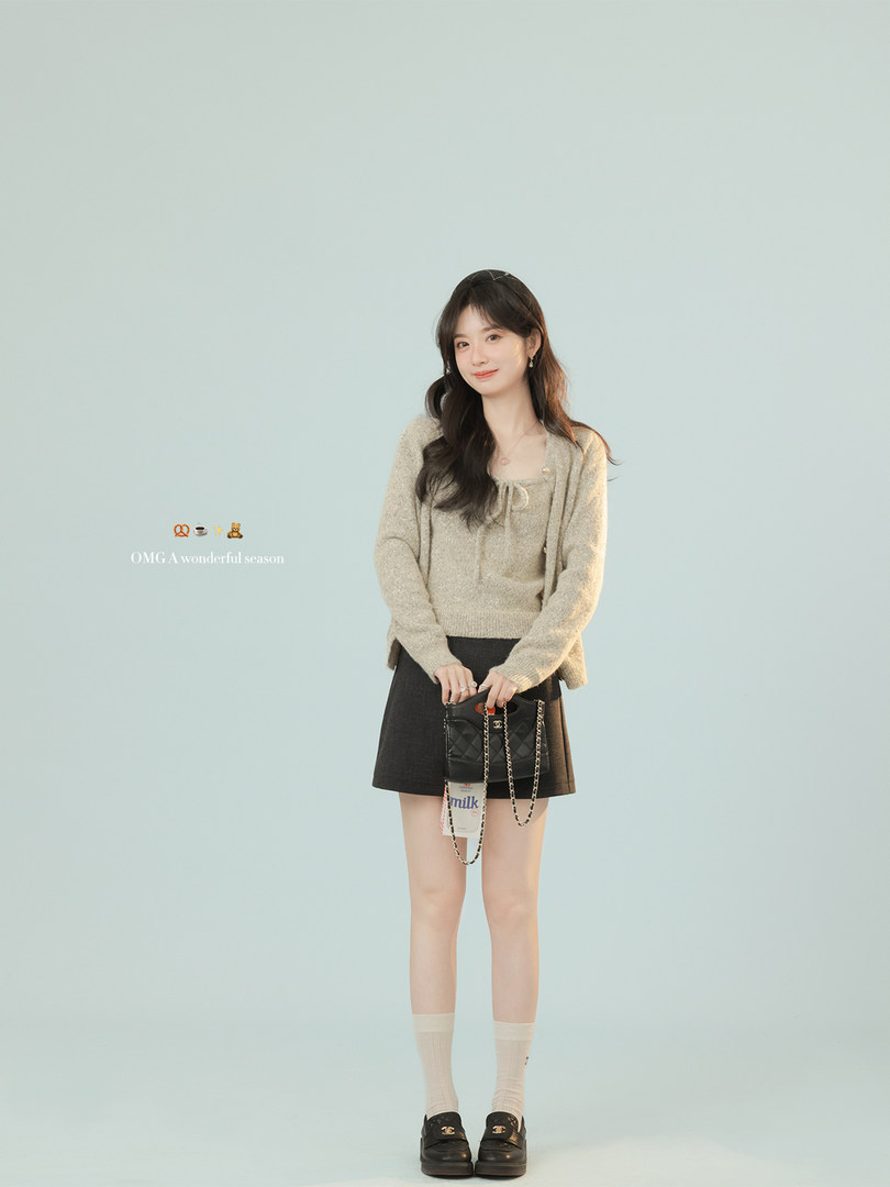 Model wearing a beige knit sweater with a black mini skirt and black loafers, holding a small black chain bag
