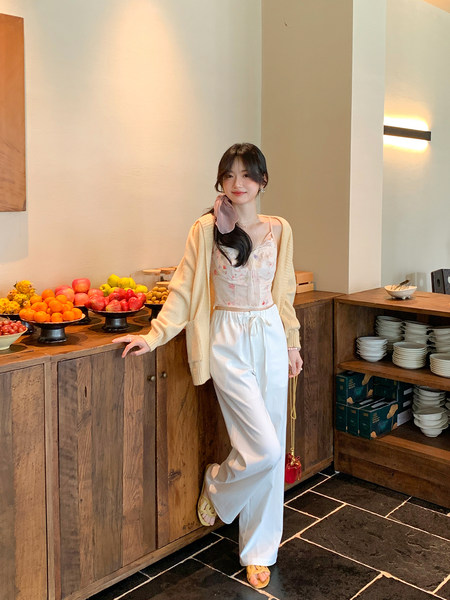 Woman wearing a light cardigan, floral camisole, white wide-leg pants, and sandals in an indoor setting