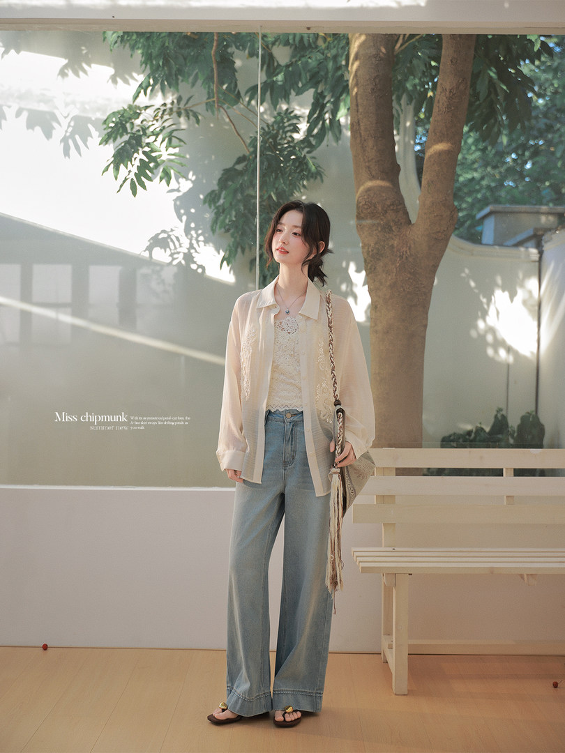 Woman wearing a light beige sheer button-up shirt with lace camisole and wide-leg jeans outdoors
