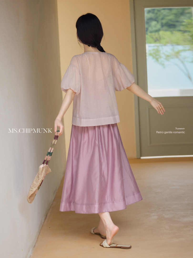 Woman wearing a light pink sheer top and matching lilac midi skirt