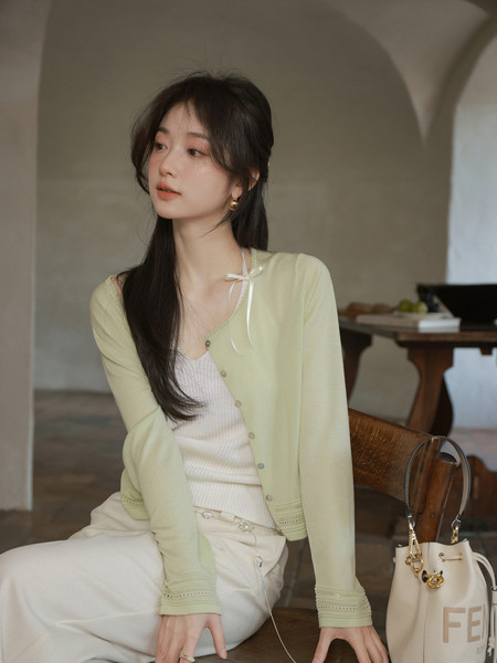 Woman wearing a light green cardigan with a white top and cream pants