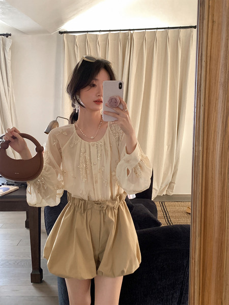 Woman wearing a sheer embroidered blouse with beige high-waisted shorts