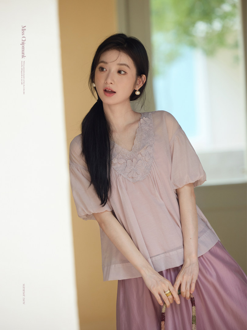 Model wearing a sheer pastel pink blouse with floral lace detail and a matching skirt