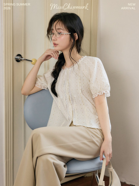 Model wearing a white lace-trim blouse with beige trousers
