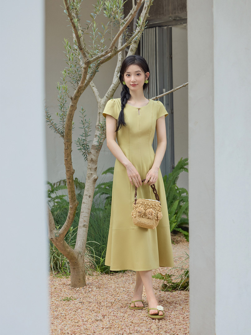 Woman wearing a light yellow midi dress and holding a woven handbag outdoors