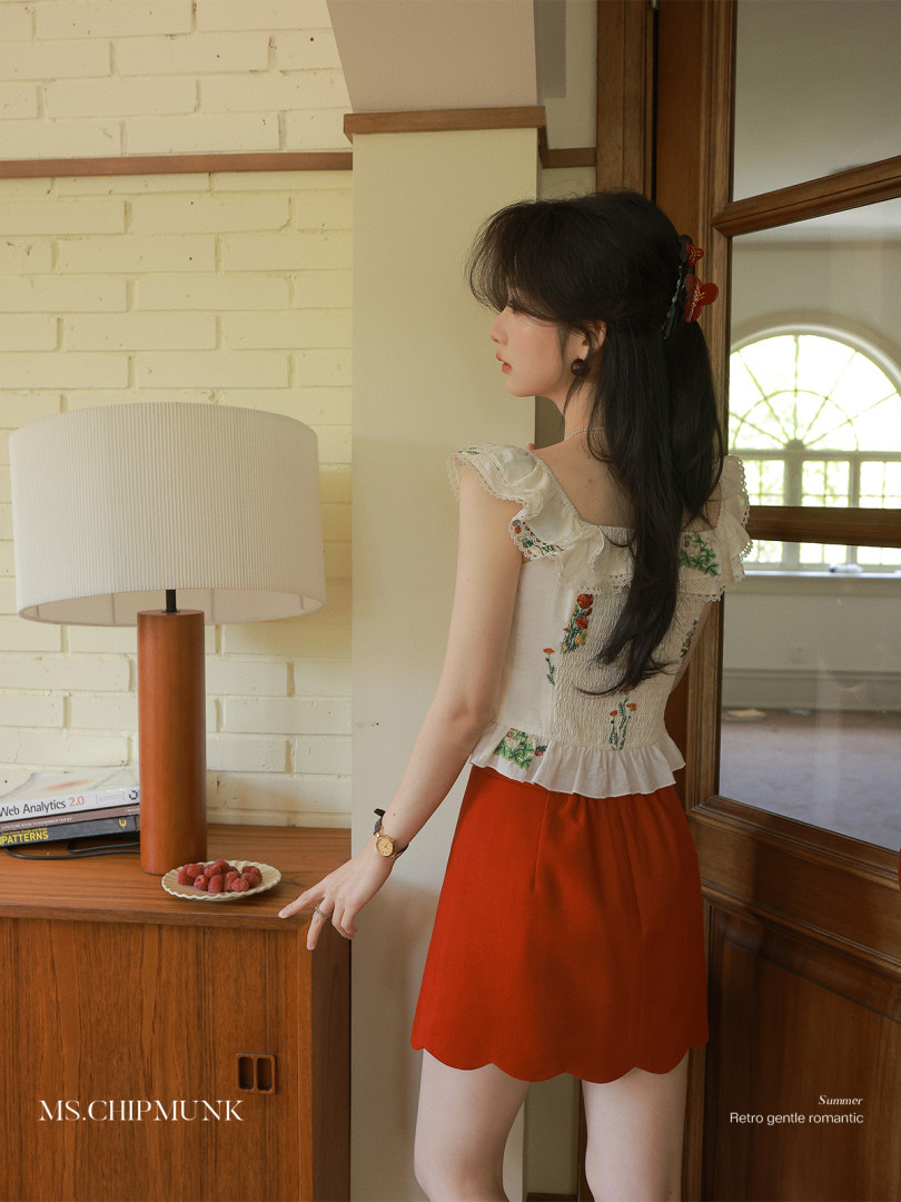Model wearing a white ruffled floral top with a bright red skirt in a summer fashion pose
