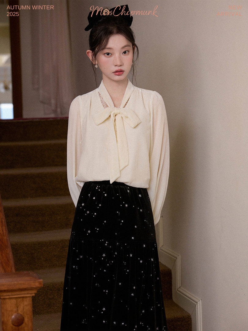 Model wearing a cream bow-neck blouse and black star-patterned skirt