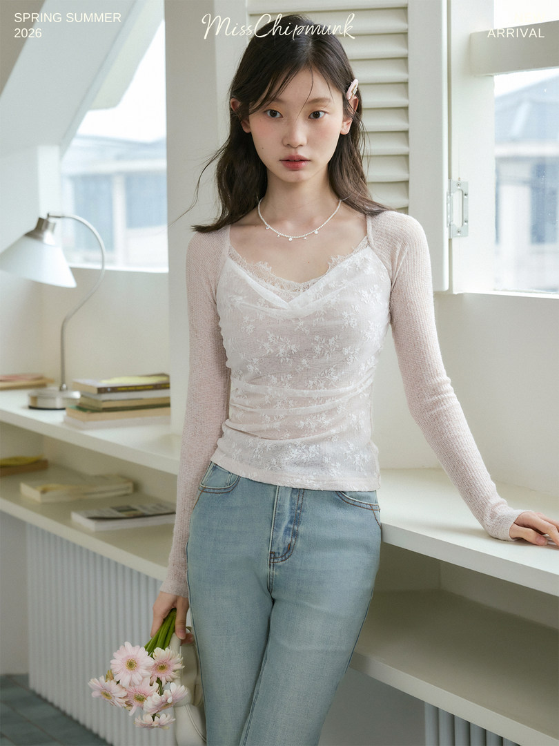 Model wearing a sheer white lace top with long sleeves and light blue jeans in a bright studio