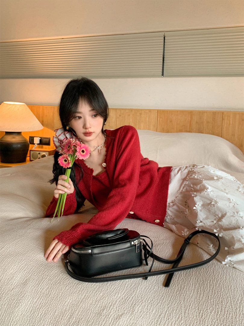Model wearing a red cardigan with a black shoulder bag on a bed