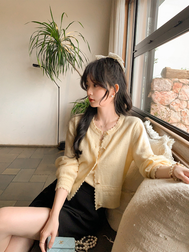 Woman wearing a cream knit cardigan with a black skirt indoors by a window
