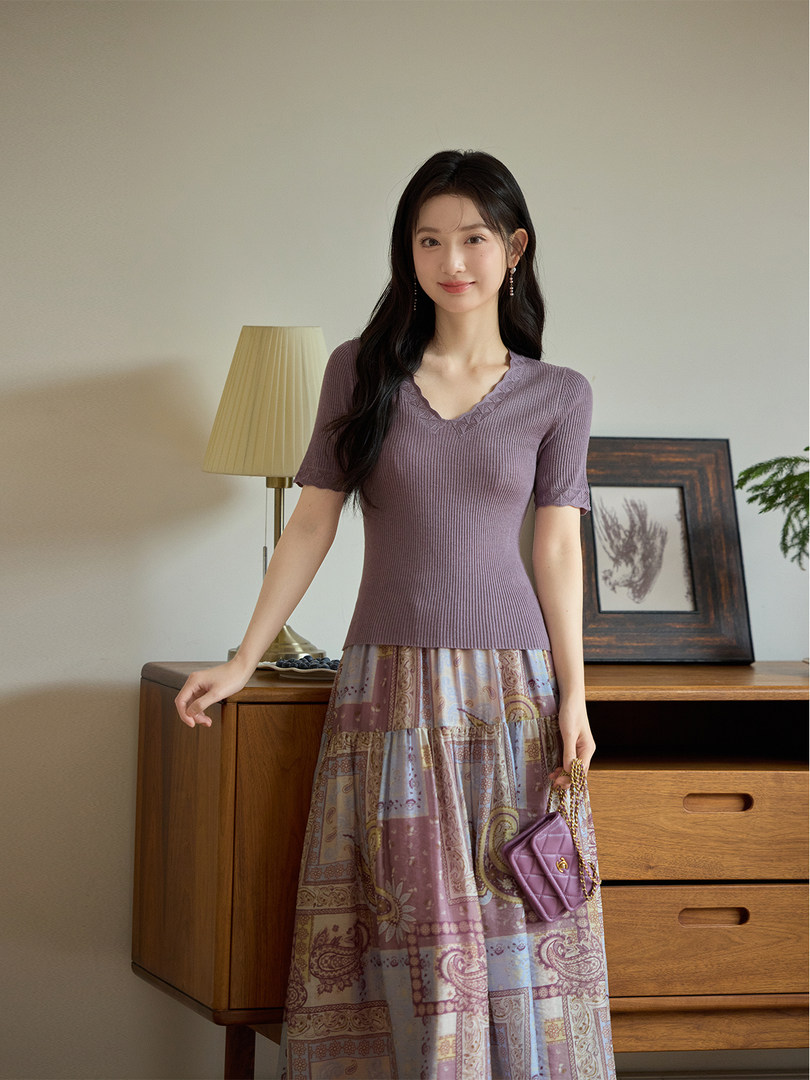 Woman wearing a purple knit top with a patterned maxi skirt and small chain bag