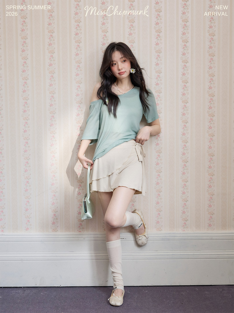 Female model wearing a pastel green top and beige wrap mini skirt