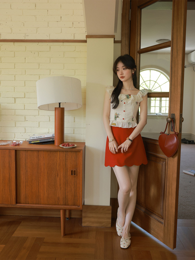 Woman wearing a floral ruffled sleeveless top with a red skirt and matching flats