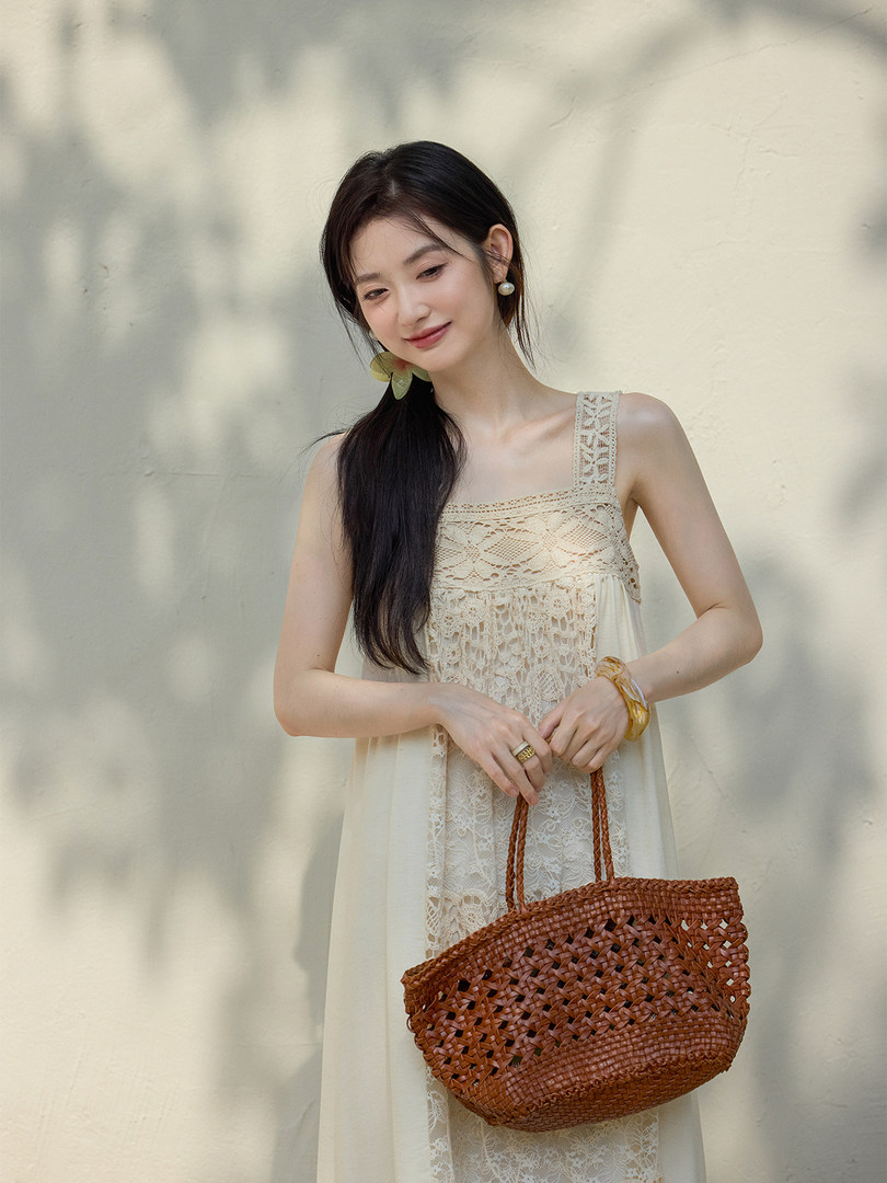 Woman wearing a cream lace dress and holding a woven brown straw bag
