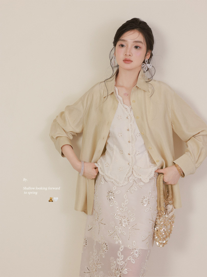 Model wearing a light beige oversized shirt over a white lace top and floral skirt