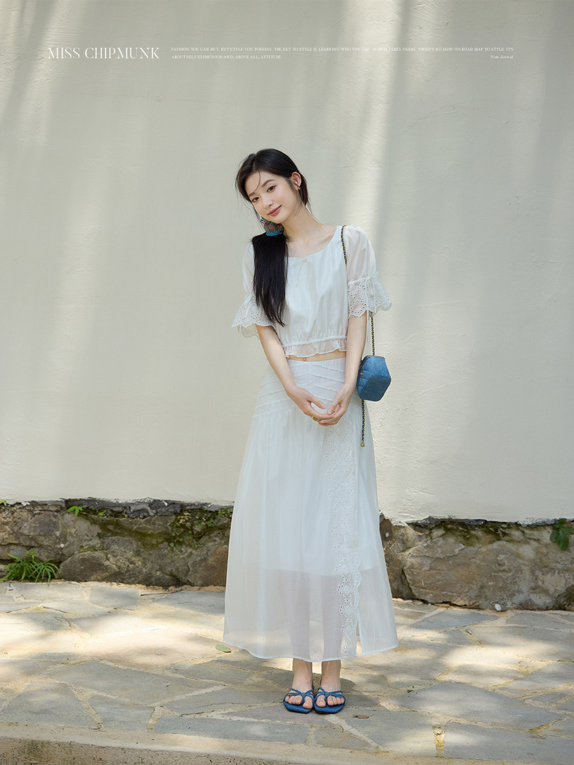 Model wearing a white sheer two-piece outfit with a long skirt and blue sandals