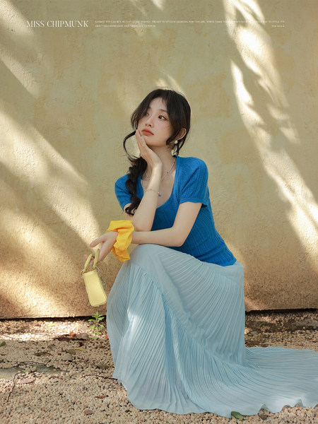 Woman wearing a blue knit top with a light blue pleated skirt and yellow handbag