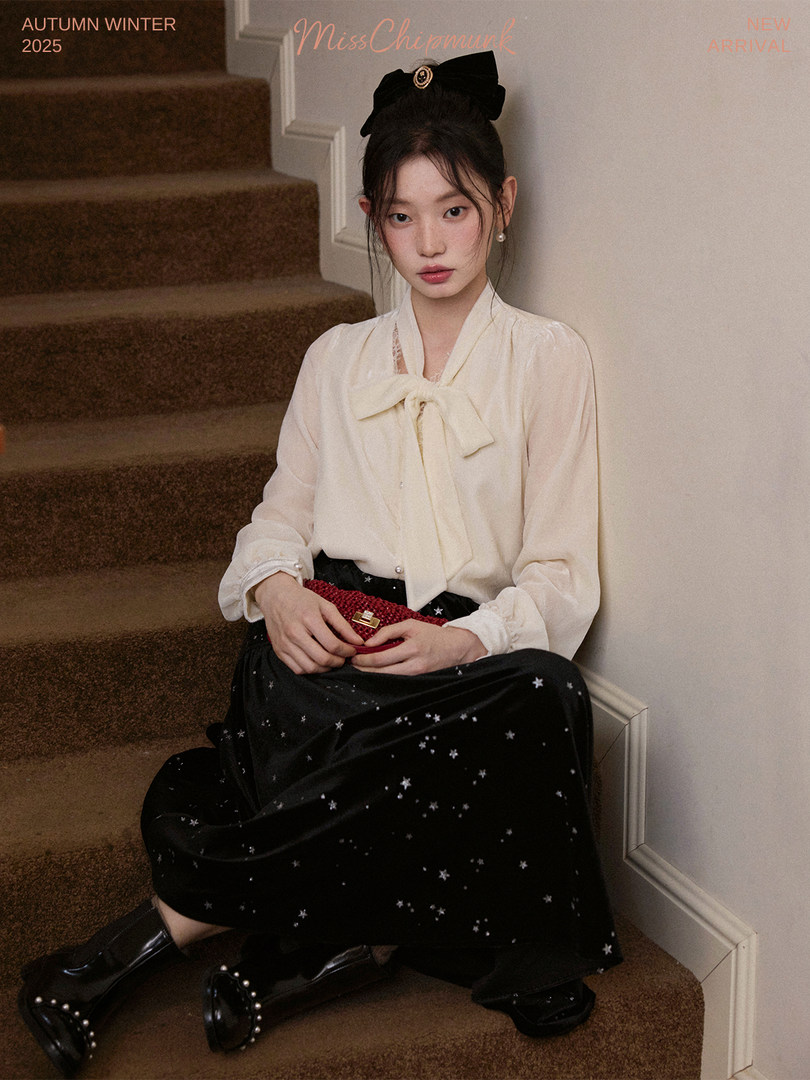 Model wearing a cream blouse and black star-print skirt in a fashion promo image