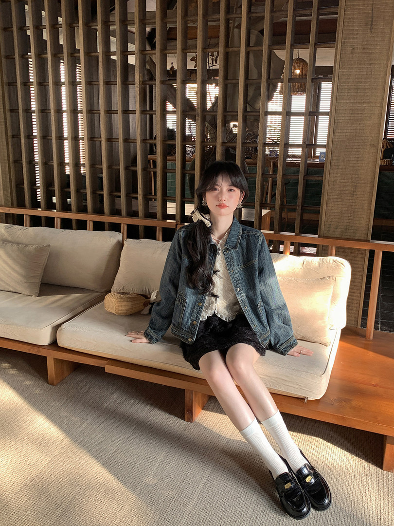 Woman wearing a blue denim jacket with a white blouse and black skirt while sitting on a sofa.
