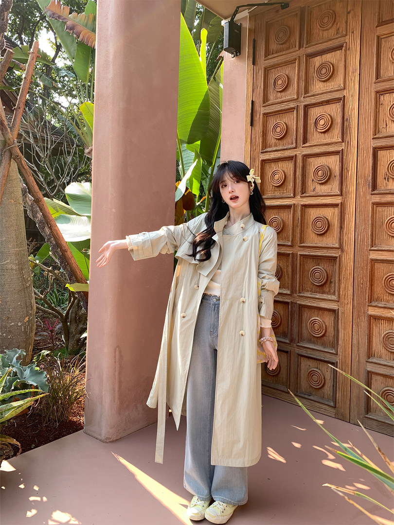 Model wearing a light beige long coat over a casual outfit