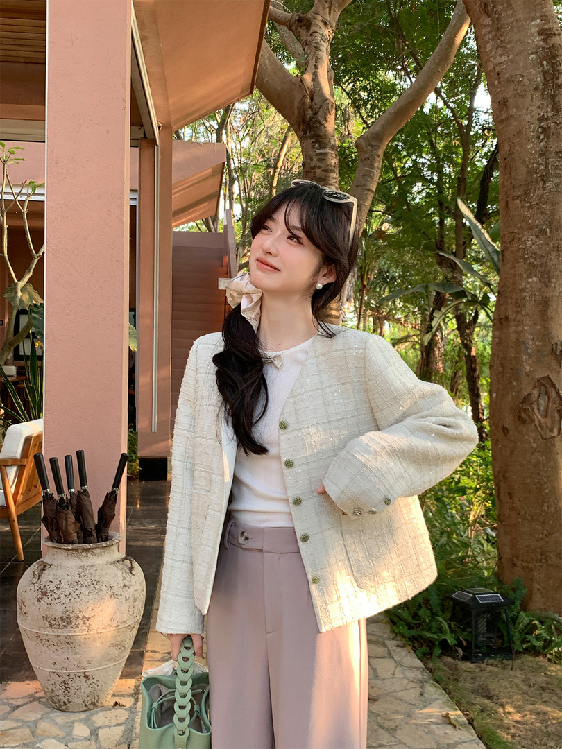 Woman wearing a white textured jacket with a white top and mauve wide-leg pants outdoors