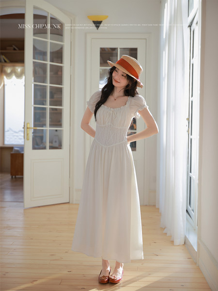 Woman wearing a white sleeveless maxi dress with a straw hat in a bright indoor setting
