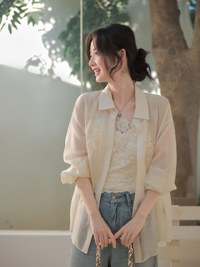 Woman wearing a sheer beige button-up shirt over a lace top with light blue jeans