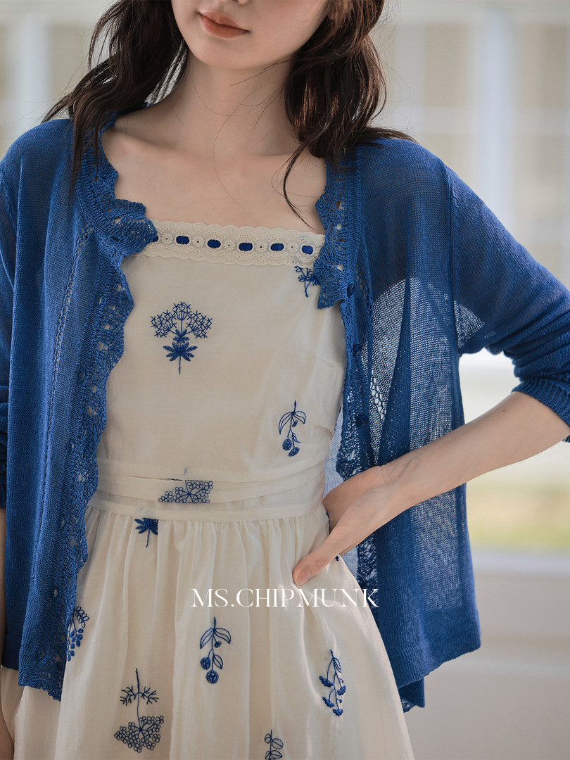 Model wearing a cream embroidered dress with a blue knit cardigan