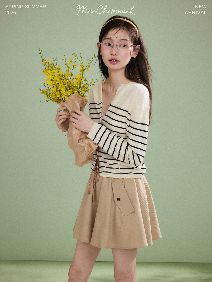 Model wearing a striped long-sleeve top and beige skirt holding yellow flowers